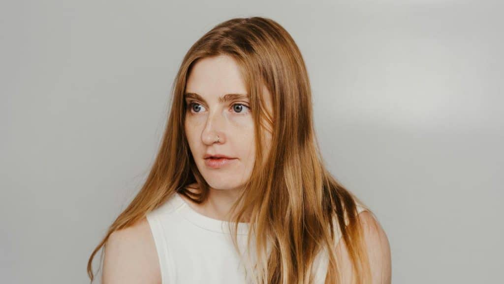 A woman with long red hair looking to the side against a plain background.