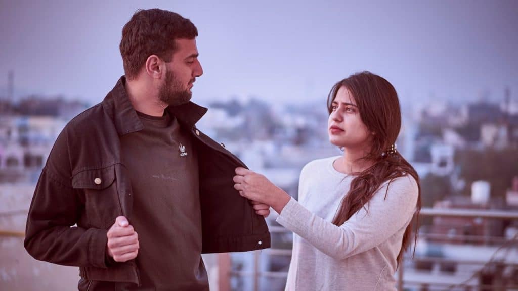 A woman holding onto a man’s jacket while they stand together on a rooftop.