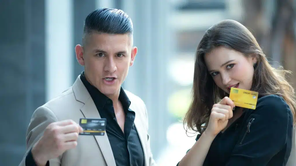 A man and woman standing outdoors holding up black and yellow credit cards toward the camera.