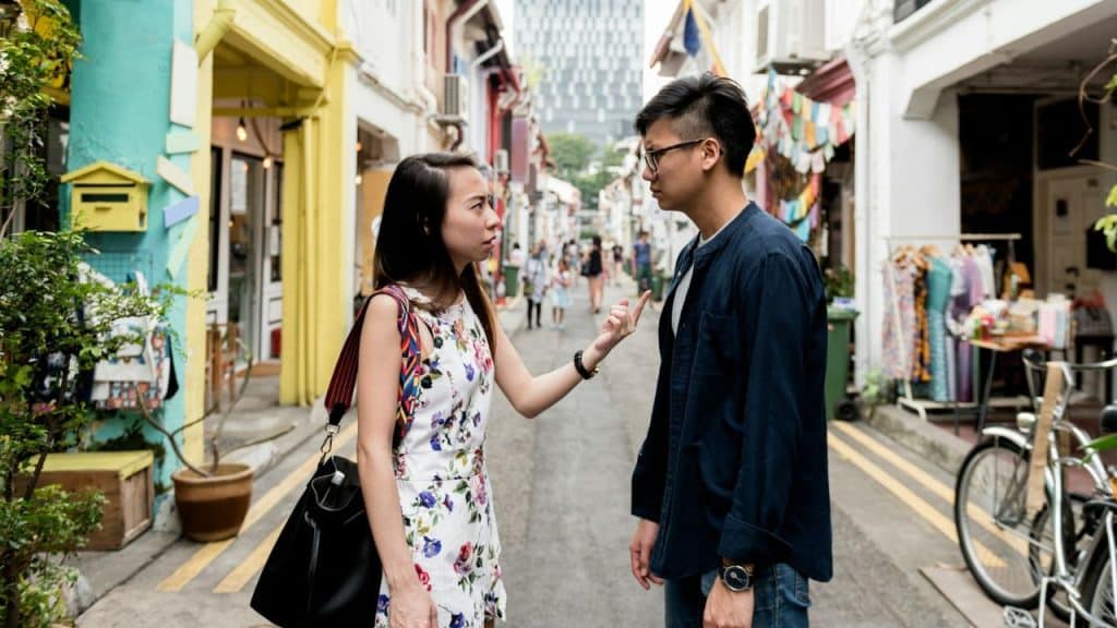 A woman points her finger while confronting a man on a narrow city street.