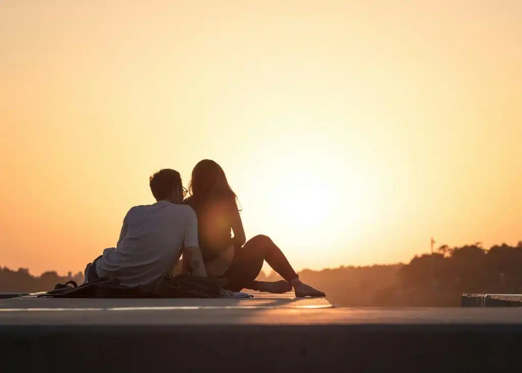 A couple sitting on a ledge watching the sunset together.