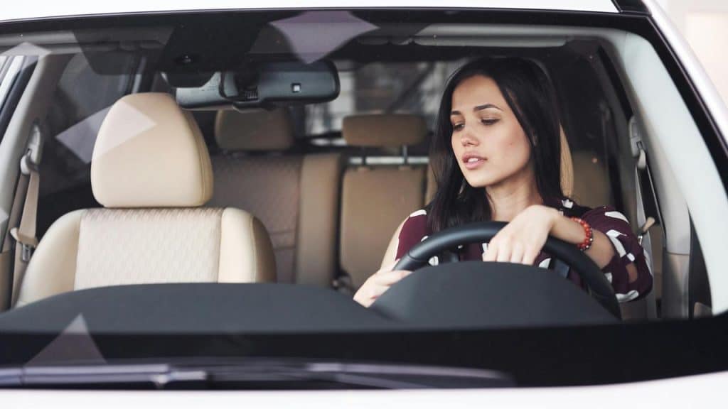 A woman sitting in the driver’s seat, holding the steering wheel inside a car.