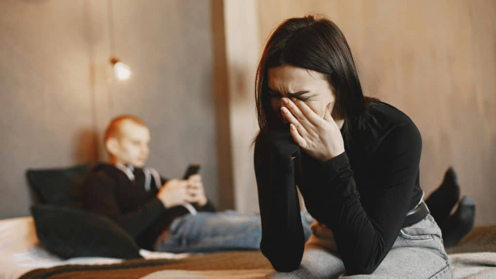 A woman cries with her hands over her face while a man sits behind her.