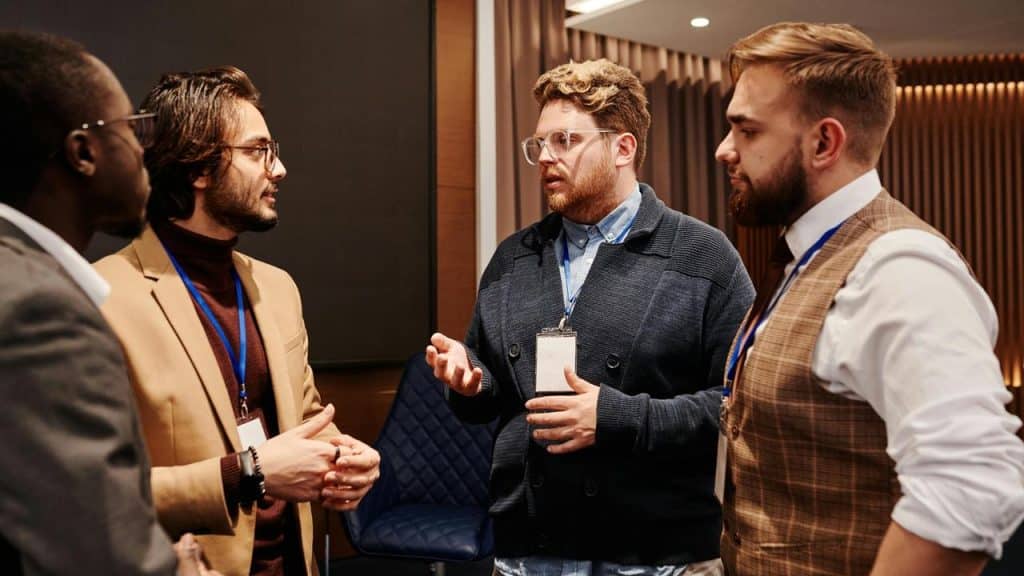 A group of men wearing badges engaged in conversation at an indoor event.