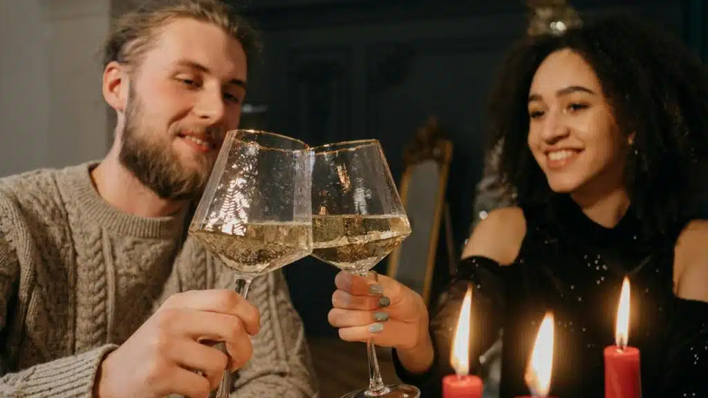 A couple smiling and clinking wine glasses at a candlelit table.