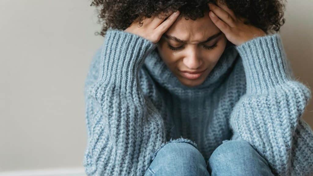 A woman sitting with her hands on her head looking distressed.