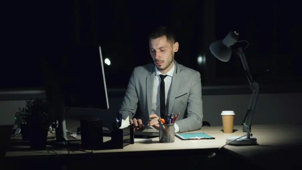 A man in a suit works at a computer in a dark office setting.