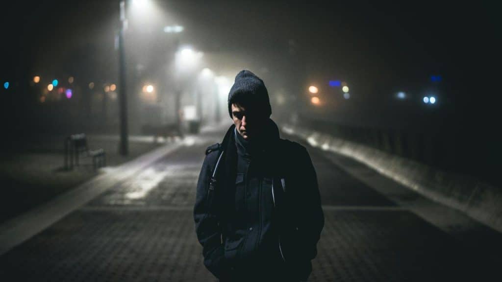 A solitary person walking down a foggy street at night under streetlights.