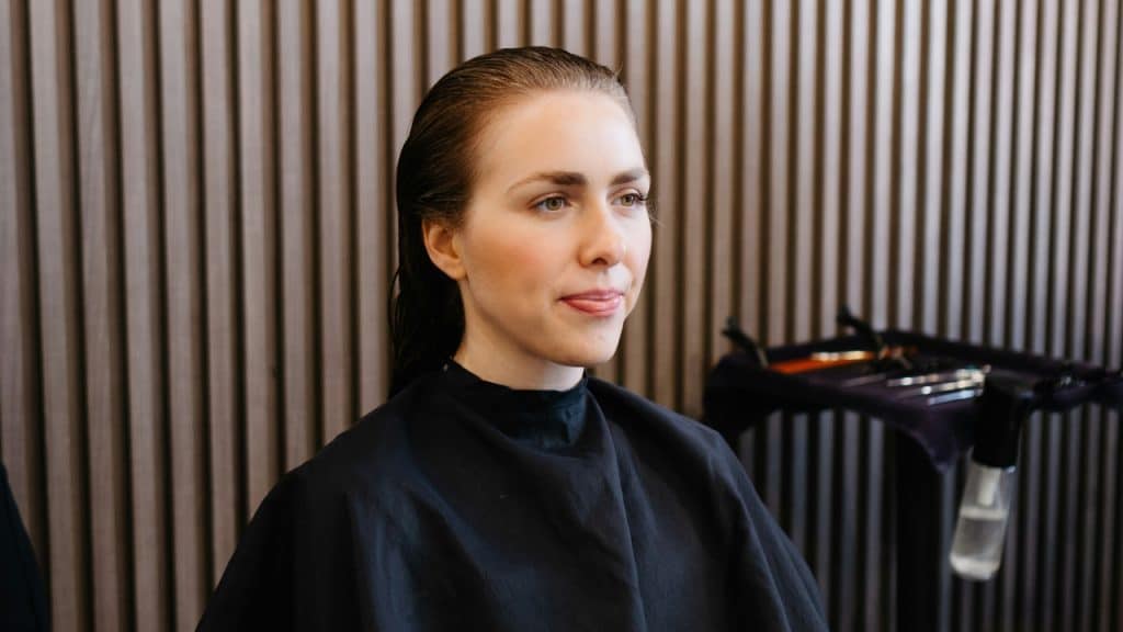 A woman with wet hair wearing a black salon cape looks toward the right side.