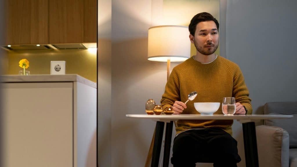 A man in a yellow sweater sits at a small table holding a large spoon.