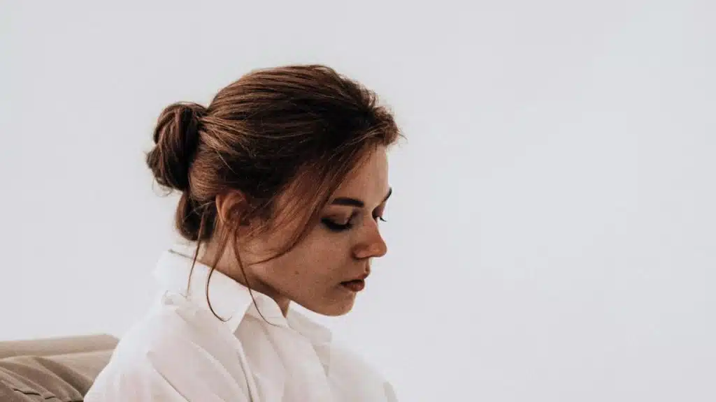 A woman with her hair in a bun looking down with a thoughtful expression.