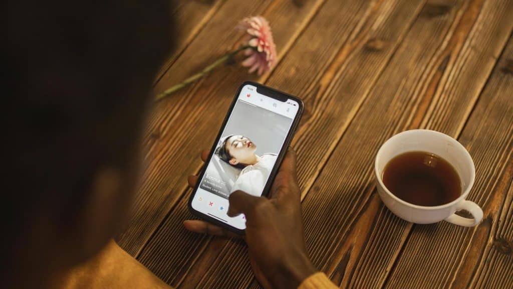 A person using a dating app on a smartphone beside a cup of tea.