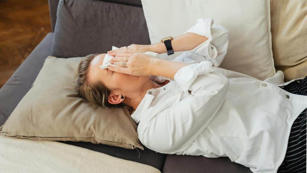 A woman lying on a couch covering her face with a tissue.