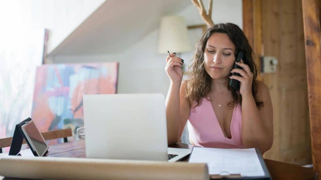 A woman talking on the phone while working on a laptop at a desk.