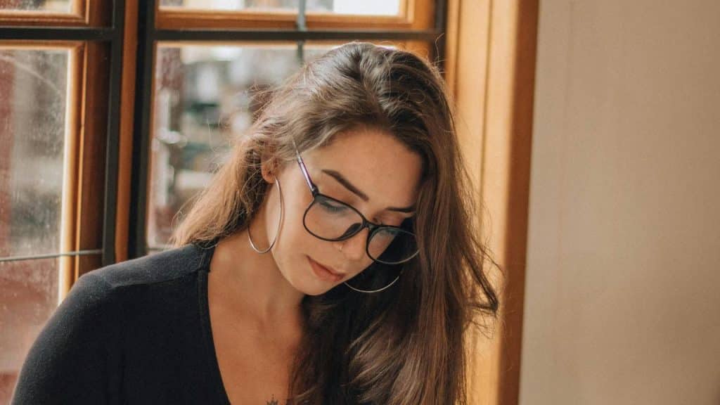 A woman wearing glasses looking down indoors.