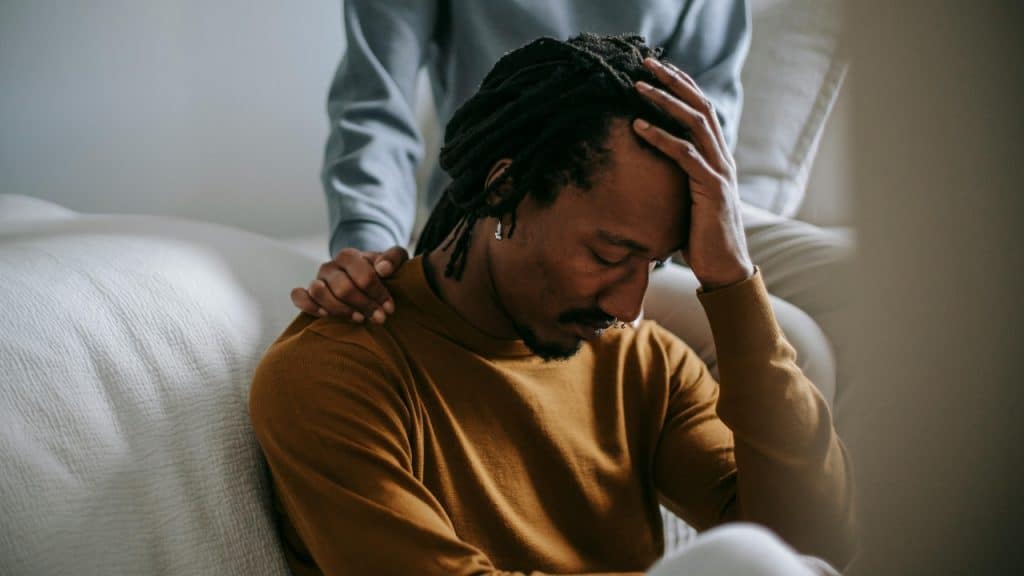 A person places a hand on the shoulder of a man holding his head.