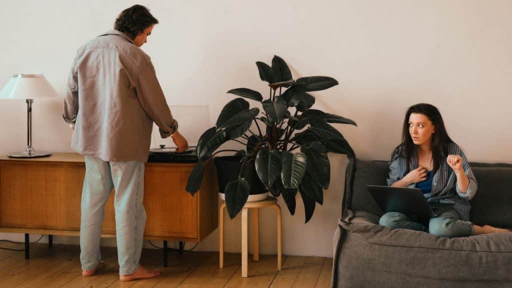 A man stands by a cabinet while a woman sits on a couch nearby.