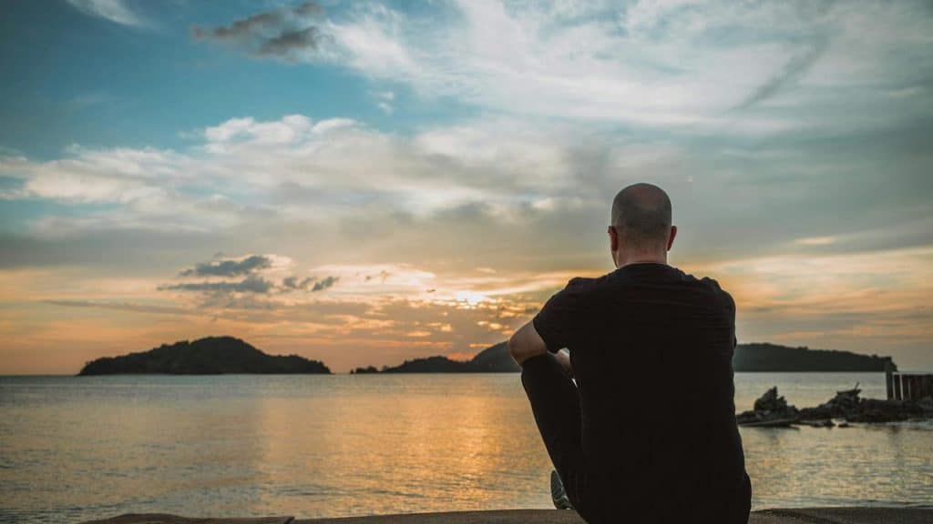 A man sitting by the water watching the sunset over distant islands.