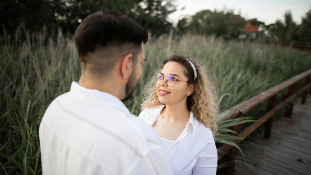 A man and woman looking at each other on a wooden outdoor walkway.