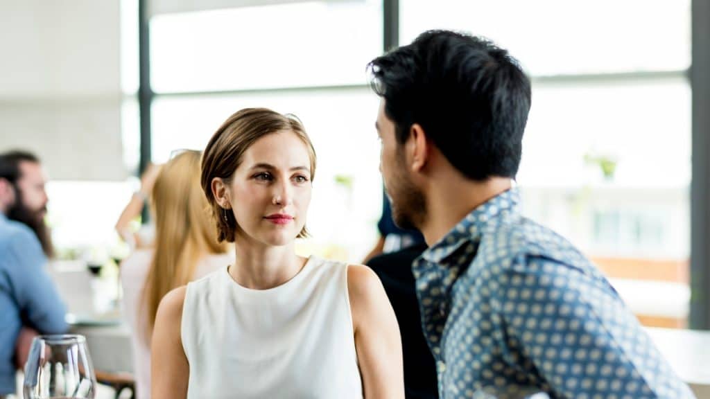 A woman looks at a man while they talk in a brightly lit room.