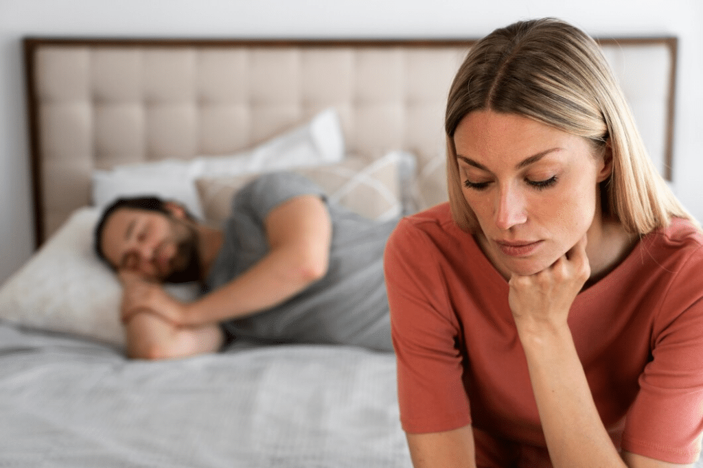 Woman sitting on edge of bed in front of sleeping husband