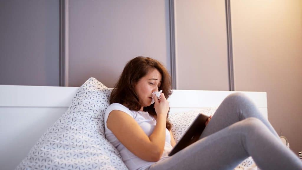 A woman sitting in bed crying while looking at a tablet.