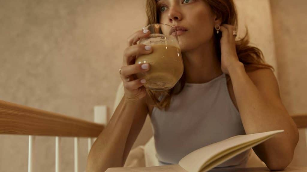 A woman drinking coffee while reading a book indoors.