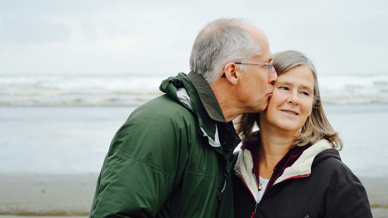A man kissing a woman beside a body of water.