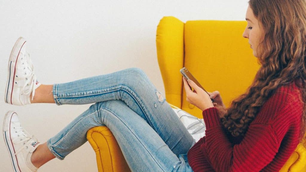 A woman sitting in a yellow chair using her phone.