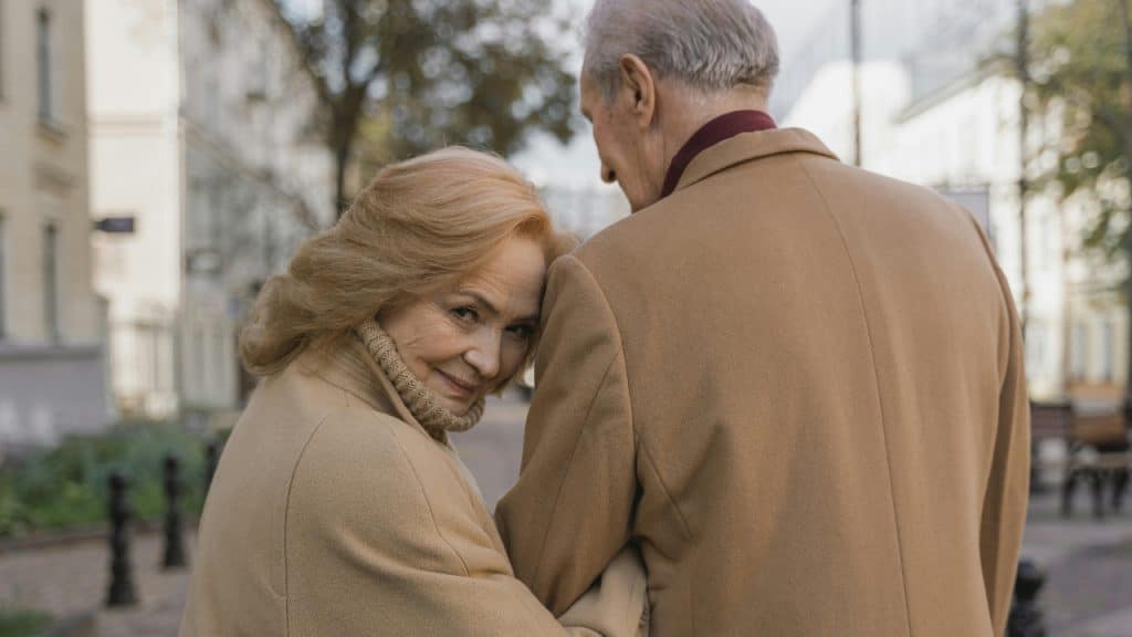 An older woman in a tan coat leans her head against a man's shoulder.