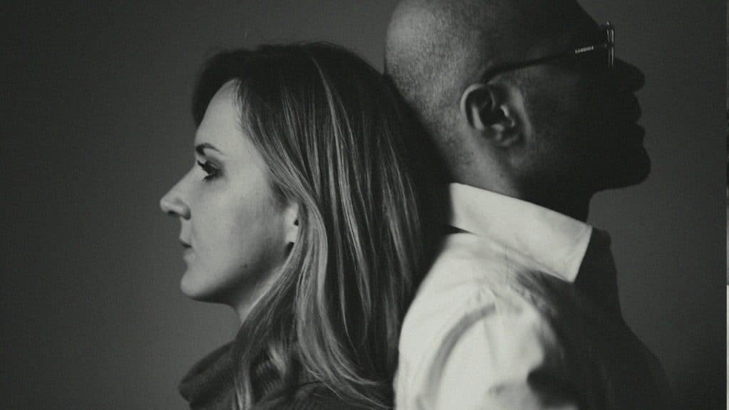 A couple standing with their backs to each other and looking in opposite directions.