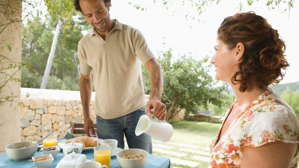 A man pouring coffee while sharing breakfast with a woman outdoors.