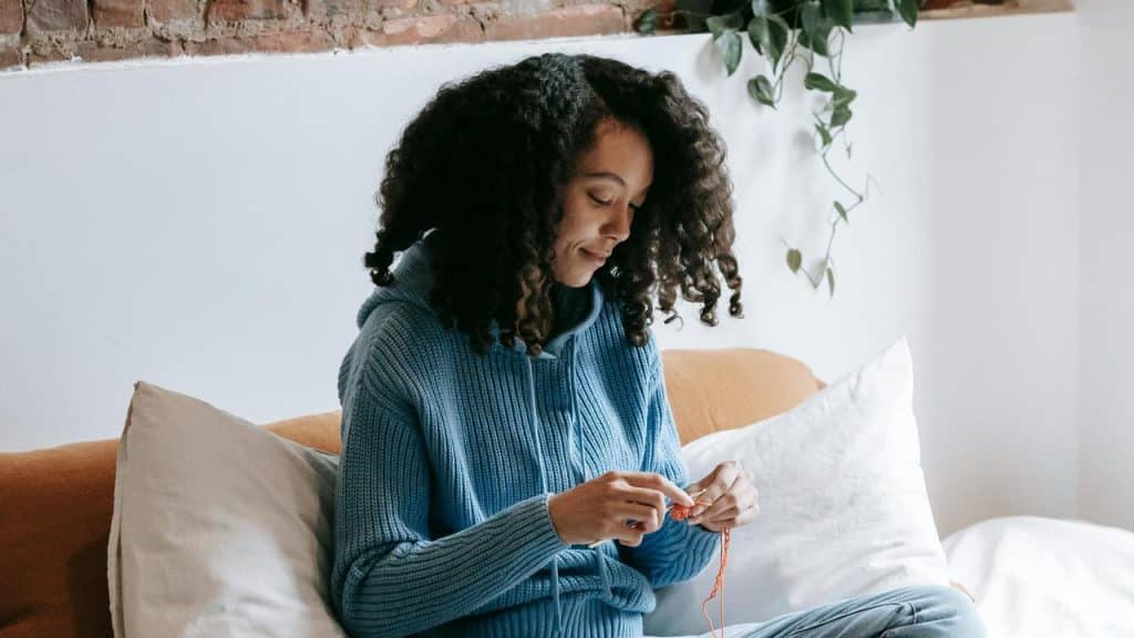 A woman knitting on a couch indoors.