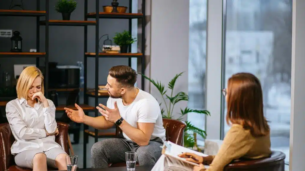 A couple arguing while a therapist listens and takes notes.