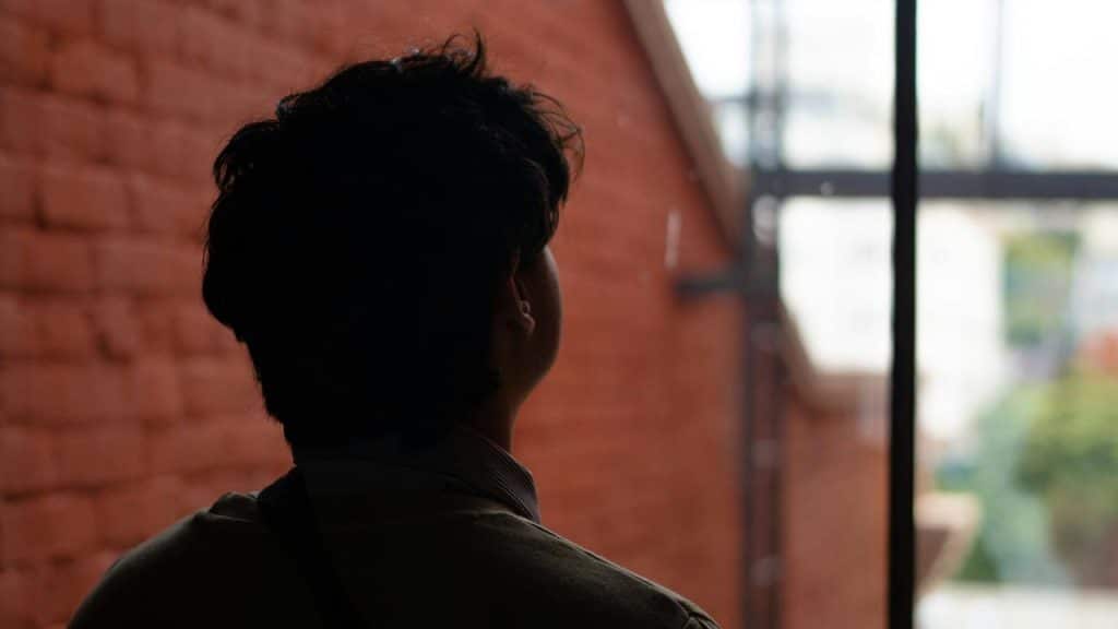 A man standing indoors looking out a window.