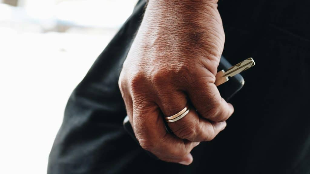 A close-up view of a person's hand holding a car key and wearing two gold rings