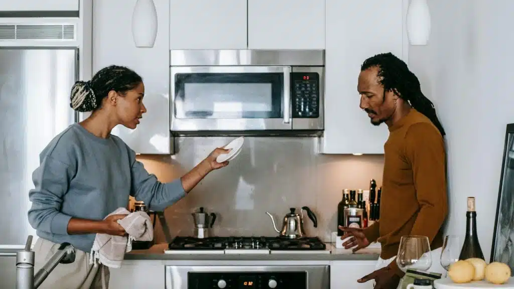 A woman holds a plate and towel while talking to a man in a kitchen.