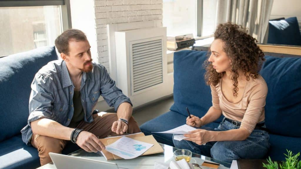 A man and woman sit on blue sofas reviewing papers and charts on a table.