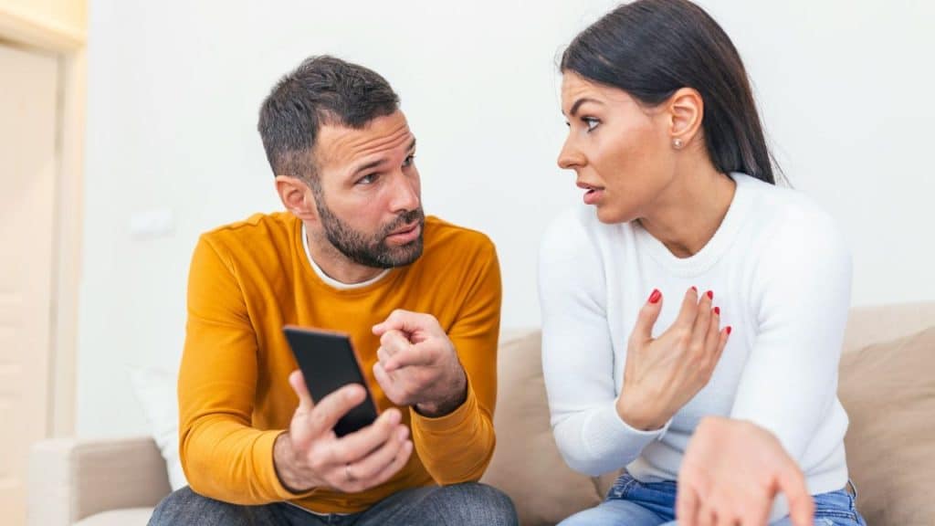 A man holds a smartphone and points his finger while speaking to a woman.