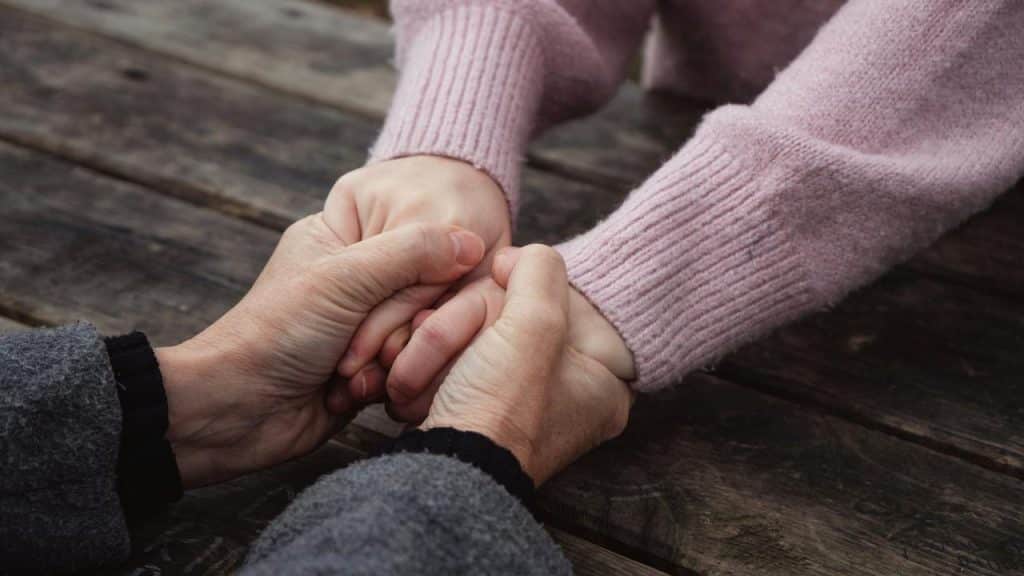 An adult gently holding another person’s hands across the table.