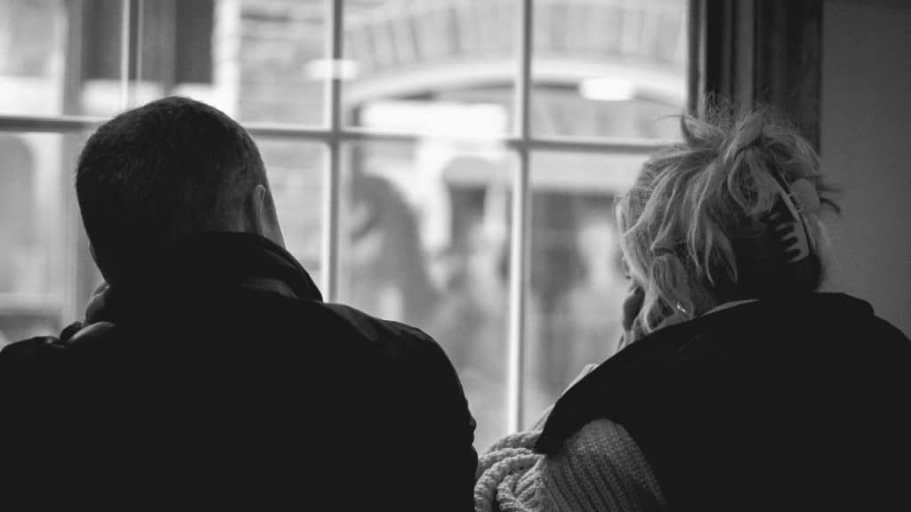 A man and woman sitting side by side, looking out a window.
