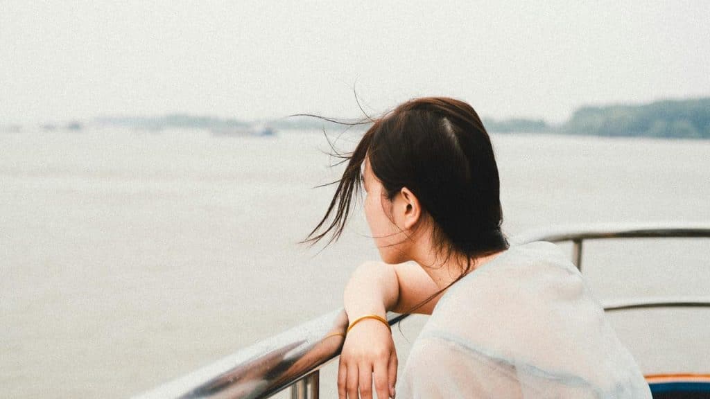 A woman leaning on a railing looking out over the water on a windy day