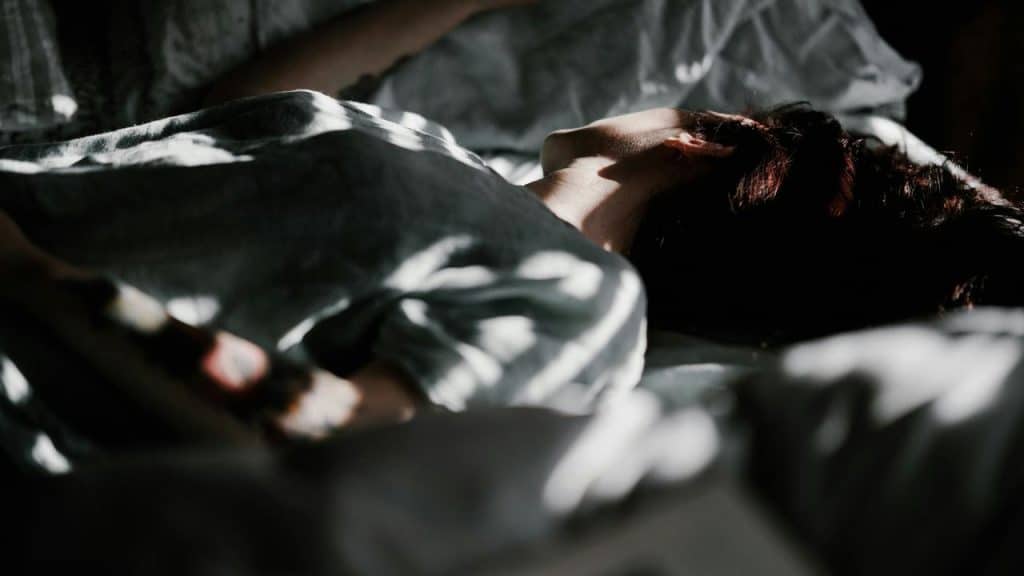 A person lies asleep in bed with sunlight casting soft shadows.