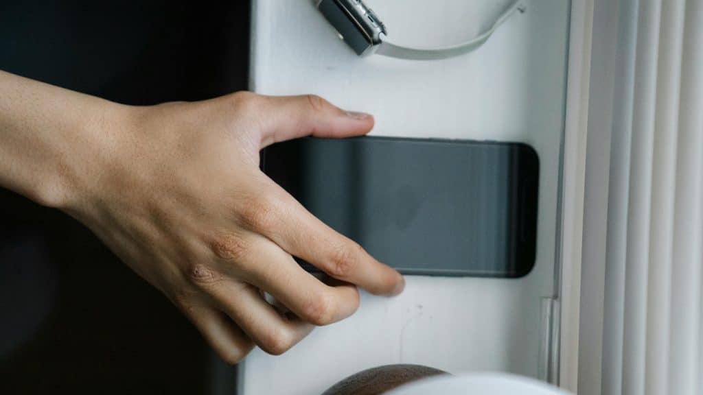 A close-up shot of a hand touching a black smartphone on a white window sill.