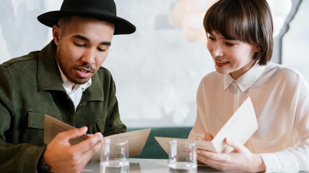 A man in a hat and a woman in a white shirt looking at menus.
