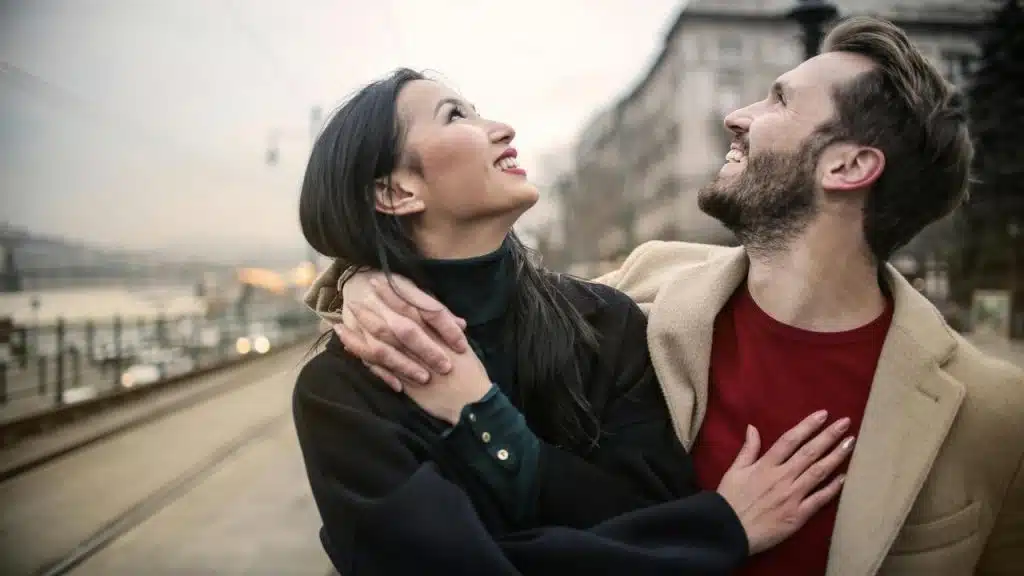 A smiling couple embracing and looking up while walking along a city street.