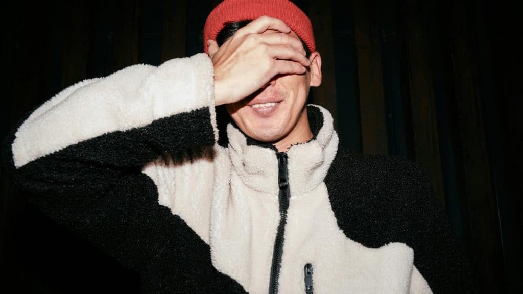 A man smiling while covering his eyes with his hand.
