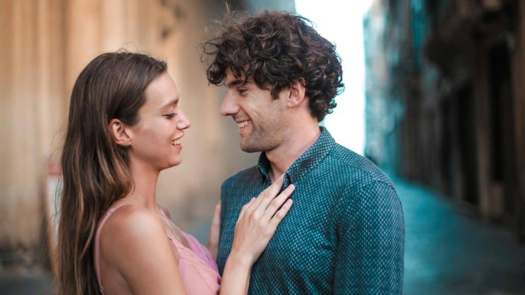A smiling couple standing close together on a city street.