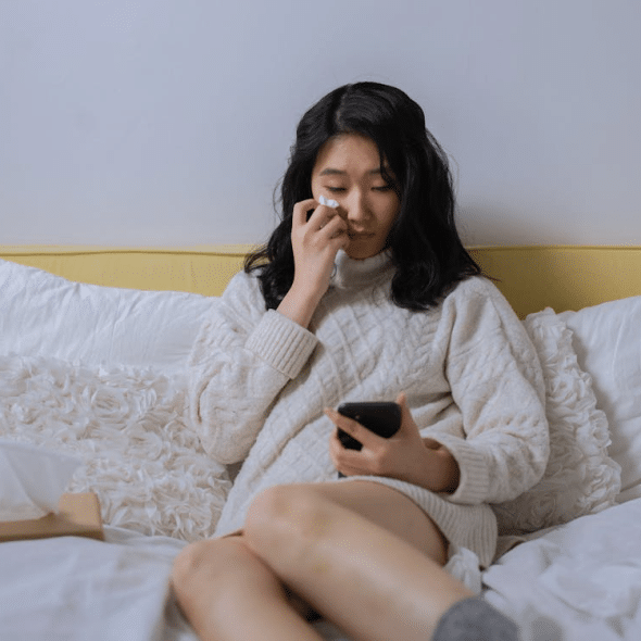 A Sad Woman Looking at her Cellphone While Sitting on a Bed
