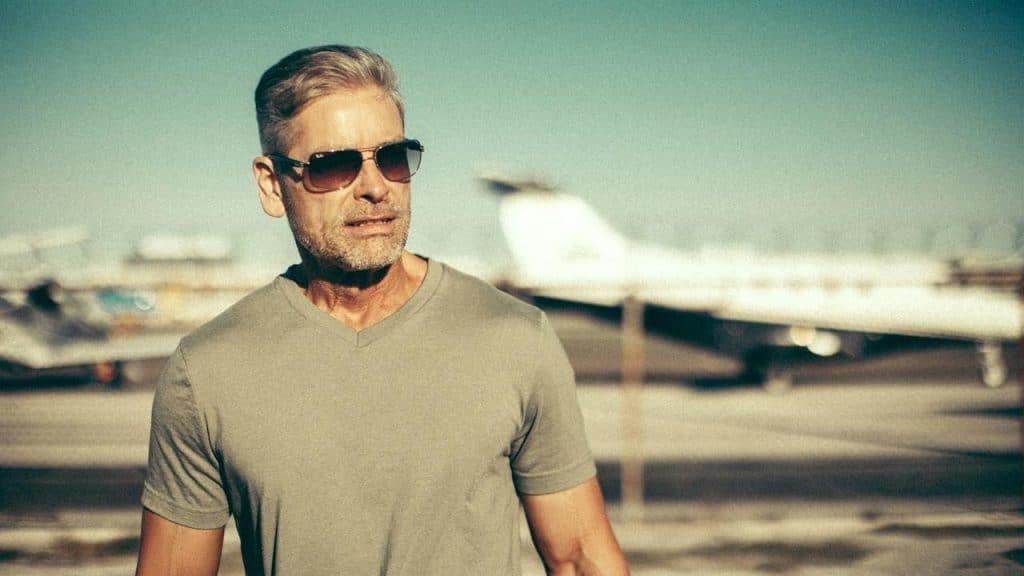 A middle-aged man wearing sunglasses and standing in an airfield.
